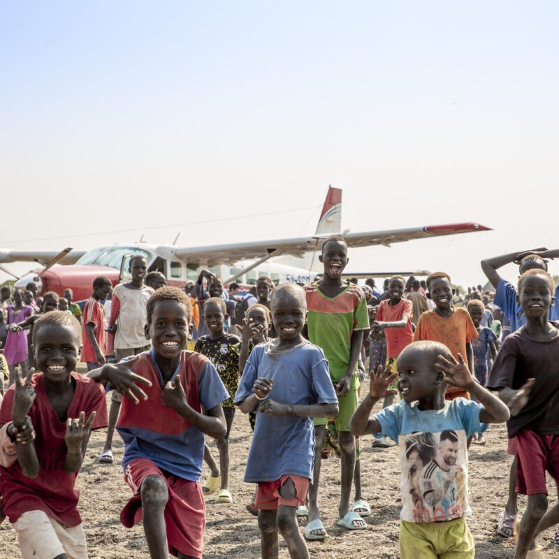 Smiling children on a beach next to an MAF plane.