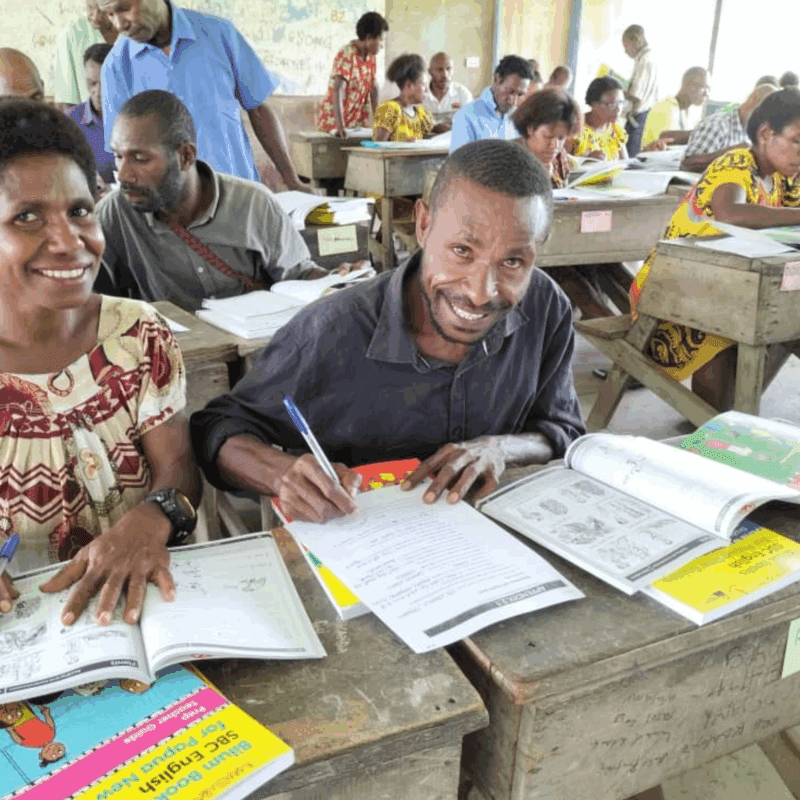 Two students sit at a desk with books in Papua New Guinea.